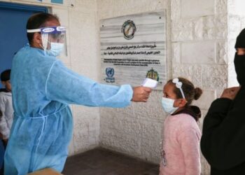 PETUGAS Pertubuhan Bangsa-Bangsa Bersatu bagi Pelarian Palestin (UNRWA) mengambil suhu kanak-kanak Palestin yang menerima suntikan vaksin Sputnik V di kem pelarian Rafah. - AFP