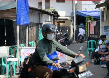 PENUNGGANG motosikal melepasi kawasan kampung di Jakarta yang dikawal selepas terdapat kes jangkitan Covid-19 dalam komuniti. - AFP