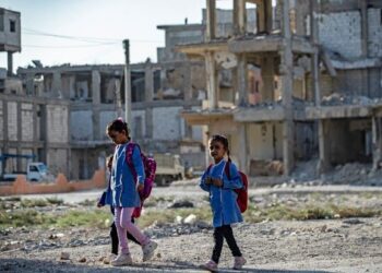 MURID sekolah berjalan di sebalik bangunan yang musnah akibat perang di Raqqa, Syria. – AFP