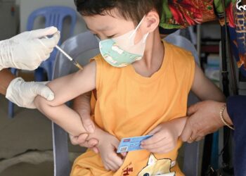 SEORANG budak lelaki melihat jarum yang dicucuk di tangannya semasa mengambil vaksin Covid-19. -AFP