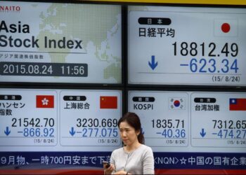 Seorang wanita melintasi paparan bursa saham Asia yang merekodkan prestasi bercampur-campur berikutan kebimbangan kenaikan inflasi global, semalam. – GAMBAR HIASAN