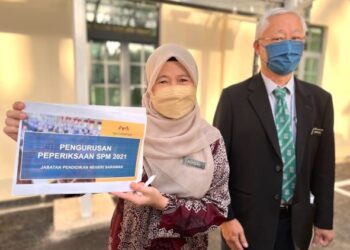 NORISAH Suhaili 
(kiri) menunjukkan set kertas pengurusan peperiksaan SPM 2021 JPNS, bersama Pengetua Sekolah Menengah Kebangsaan St. Joseph, Henry Chai (kanan) di perkarangan sekolah di Kuching hari ini.