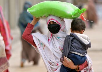 SEORANG wanita mendukung anaknya sambil mengangkat beg tepung percuma yang diterima dari pusat pengedaran kerajaan di Islamabad kelmarin.-AFP