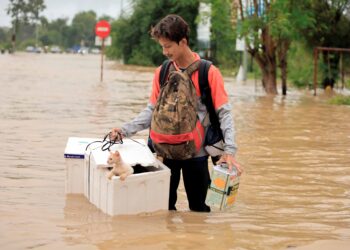 SEORANG lelaki mengharungi banjir bersama kucing peliharaannya di Lubok Jong, Pasir Mas, Kelantan, bulan lalu. – UTUSAN/KAMARUL BISMI KAMARUZAMAN
