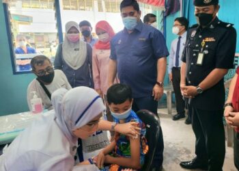 SHAHELMEY Yahya (berdiri-dua kanan) melihat proses pemberian vaksin di SK Kg Contoh, Putatan hari ini.
