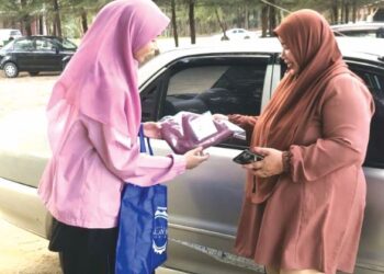 HANIM Sophia Mohd. Sohor (kiri) mengagihkan tudung secara percuma kepada wanita di bandar Marang, Terengganu.