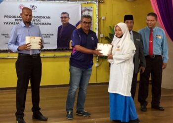 MOHD Razman Yaakob menyerahkan bantuan cermin mata kepada salah seorang pelajr pada Program CSR Pendidikan Pesisir Pantai di SMK Baru Rakit, Kuala Nerus, Terengganu, hari ini. - UTUSAN/TENGKU DANISH BAHRI TENGKU YUSOFF