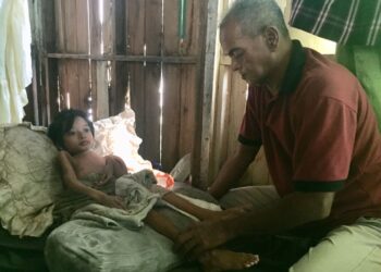 ISMAIL Wahab sentiasa menemani  Muhammad Hafizzudin yang terlantar di rumah di Kampung Lorong Haji Da, Batu Buruk, Kuala Terengganu. – UTUSAN/TENGKU DANISH BAHRI TENGKU YUSOFF