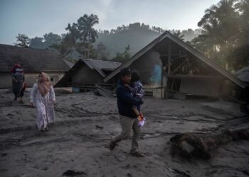 SEORANG lelaki membawa keluarganya keluar dari kawasan rumah yang ditenggelami lumpur letusan gunung berapi Gunung Semeru di kampung Kajar Kuning di Lumajang semalam.-AFP
