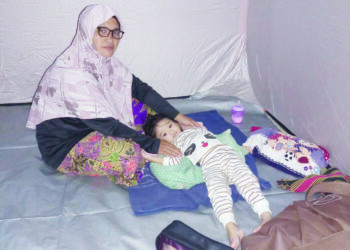 MASHITAH Ahmad bersama cucunya berlindung di PPS Dewan Terbuka Kampung Padang Empang selepas rumahnya dinaiki air di Kupang, Baling, Kedah petang kelmarin. – UTUSAN/NORLIA RAMLI