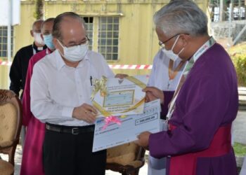 Douglas Uggah (kiri) menyampaikan cek untuk dana Katedral St Thoms kepada  Danald Jute di Kuching hari ini.