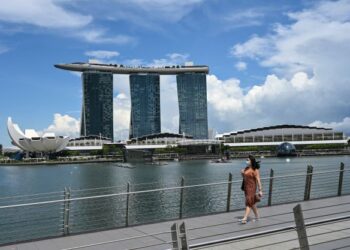 PENDUDUK sedang berjalan di sebuah jambatan berlatar belakang Marina Bay di Singapura. - AFP