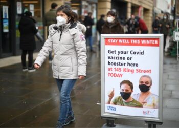 SEORANG wanita berjalan melintasi papan tanda peringatan suntikan dos penggalak vaksin Covid-19 di London, Britain. - AFP