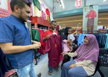 MOHAMAD Shauti Zakaria (tengah) yang ditemani Murtadhatumizi Mustapha (kiri) memegang baju Melayu pilihannya semasa dibawa membeli pakaian baharu untuk menyambut kedatangan Hari Raya Aidilfitri di Kota Bharu, Kelantan. - UTUSAN/YATIMIN ABDULLAH