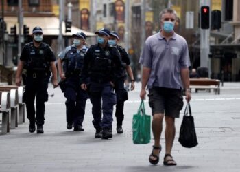 SEORANG lelaki melintasi anggota polis yang mengawal laluan di Sydney. -AFP