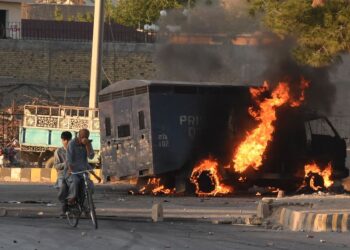 DUA lelaki melalui sebuah kenderaan polis yang rentung dibakar penunjuk perasaan di bandar Quetta, Pakistan.-AFP
