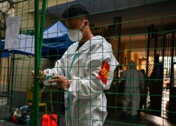 PETUGAS mengunci kawasan perumahan penduduk semasa perintah berkurung di daerah Xuhui, Shanghai.-AFP