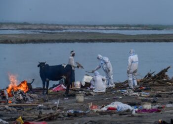 AHLI keluarga memakai sut perlindungan diri (PPE) melakukan beberapa ritual dalam upacara pembakaran mayat mangsa Covid-19 di tebing Sungai Ganges. - AFP