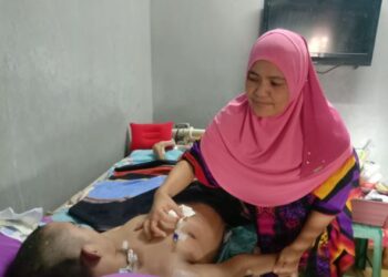 SAPIDAH Sahed membetulkan saluran makanan dipasang pada badan Mohd. Zaki Hanfi yang koma sejak lima tahun lalu.