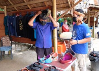 ARIFFIN Deraman (kiri) mencuba tengkolok yang dipamerkan di gerai jualan di Kalang Warisan di Kuala Terengganu hari ini. - PUQTRA HAIRRY ROSLI