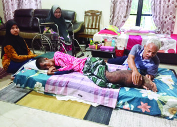 RAMLI Mamat (kanan) sambil menggosok kaki anak bongsunya yang besar akibat penyakit ‘kaki gajah’ bagi mengurangkan rasa lenguh dan turut diperhatikan isterinya, Murni Md. Daud (tengah) dan Nor Aliah Safiah (kiri) di kediamannya di Kampung Bukit Palas, Cherating di Kuantan, Pahang. - UTUSAN/DIANA SURYA ABD WAHAB