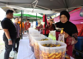 ROHANI Hashim (kanan) membungkus jeruk dibeli pelanggan di gerainya di Kampung Cabang Empat Cherang, Kota Bharu, Kelantan. - UTUSAN/KAMARUL BISMI KAMARUZAMAN