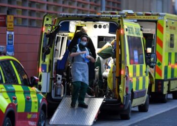 PASUKAN paramedik berada bersama pesakit di dalam ambulans yang diparkir di luar sebuah hospital di London. - AFP   