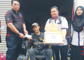 BAHARUDIN Abu (kiri) menyerahkan sumbangan kepada Muhammad Farid Hilmy Mohd. Nasir (berkerusi roda) di sebuah bengkel di Seksyen 7, Shah Alam, Selangor. – UTUSAN/ISKANDAR SHAH MOHAMED