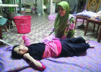 SITI Hajar Hasan melihat keadaan Siti Hawa Baharum yang lumpuh akibat sawan di Kampung Kemat. – MINGGUAN/NOOR HAYATI MAMAT