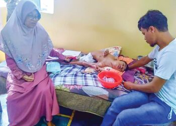 SHAMIL Ahmad (kanan) mengusap kepala kembarnya, Shamrin yang terlantar sambil diperhatikan ibu mereka, Che Rohyana Manap semasa ditemui di Taman Permatang Katong, Kota Kuala Muda di Sungai Petani. – UTUSAN/OTHMAN YAHAYA