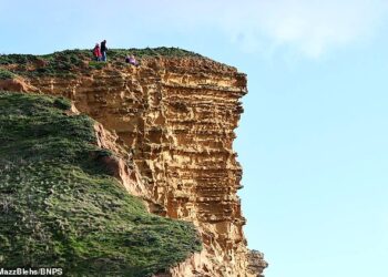 SEORANG lelaki mengambil gambar anaknya di atas tebing setinggi 45.72 di West Bay, Dorset, England. - AGENSI