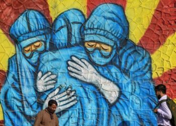 PENDUDUK berjalan melepasi lukisan mural menunjukkan petugas kesihatan memakai sut PPE untuk menyebarkan kesedaran mengenai pandemik Covid-19 di Mumbai. - AFP