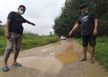 DUA wakil penduduk menunjukkan jalan yang berlubang dan berlopak di Jalan Ladang Kampung Tehel Ulu, Tehel, Melaka. - UTUSAN/MUHAMMAD SHAHIZAM TAZALI