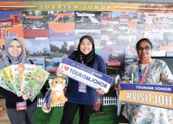 NUR Aisyah Syahmienna Mohd. Razip (tengah) bersama petugas Tourism Johor menunjukkan risalah pelancongan sempena FMJ 2022 di Puteri Harbour, Iskandar Puteri, Johor.