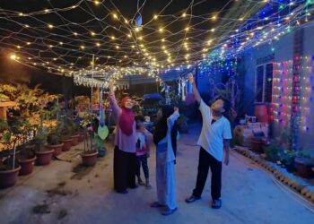 SEBUAH keluarga bersantai di hadapan rumah yang diwarnai hiasan dan cahaya lampu di Felda Kota Gelanggi Dua di Jerantut, Pahang. - UTUSAN/HARIS FADILAH AHMAD