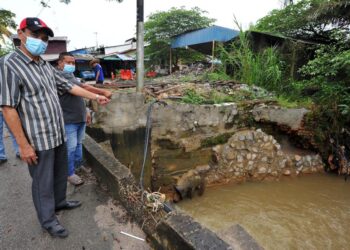 SABARUDIN Burahan (kiri) bersama Adli Suri Rabu menunjukkan tembok batu yang dibina sendiri penduduk kampung bagi mengelak berlakunya kejadian tebing runtuh akibat hakisan berpunca daripada banjir di Kampung Bukit Pulai, Pasir Gudang di Johor. -UTUSAN/RAJA JAAFAR ALI