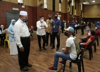 ROZALI Mohamud (kiri) bertanyakan sesuatu kepada seorang peniaga yang sedang menunggu giliran untuk divaksin di Pusat Pemberian Vaksin (PPV) SP Arena di Seberang Jaya, Pulau Pinang hari ini.