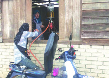 SURAYA Abdullah mengisi minyak petrol kepada pelanggannya dengan menggunakan pam minyak tradisional di Dabong, Kuala Krai, Kelantan. - UTUSAN/ROSMIZAN RESDI