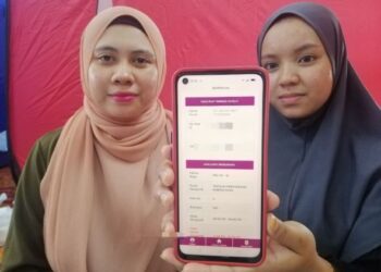 SITI Aisyah Zuhariman (kiri) menunjukkan rekodnya sebagai pengundi PRU15 di PPS SK Kubang Kuau, Rantau Panjang, Kelantan. - UTUSAN/ROHANA ISMAIL