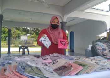 FARAHWAHIDA Ramli menunjukkan pelbagai jenis kain tudung yang dijual untuk wanita persiapan Hari Raya Aidilfitri di pekan Kerambit di Lipis, Pahang. - UTUSAN/HARIS FADILAH AHMAD