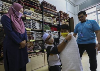 ZULKIFLI Muhamed  memakaikan kain ihram pada Muhammad Danish Riza Hadi sambil diperhatikan Noor Herra Hardiana Badri di Senawang, Seremban. – UTUSAN/NOR SHAFAWATI YUP