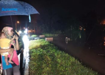 NOR Karziela Sulong mendukung anaknya berusia tujuh bulan melihat keadaan banjir yang menenggelamkan rumah mentuanya di Kampung Pilin, Rembau, Negeri Sembilan, malam ini. - UTUSAN/NOR AINNA HAMZAH