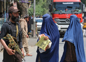 DUA wanita Afghanistan yang lengkap memakai burka berjalan di depan anggota keselamatan Taliban di Jalalabad. - AFP