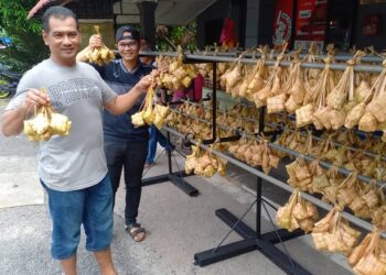 MUHAMMAD Yusri Mahat (depan) dan anaknya, Ezrul Syafiq menunjukkan ketupat daun kelapa atau ketupat nasi yang sudah dimasak di Kampung Padang, Jalan Pokok Mangga, Melaka. - UTUSAN/AMRAN MULUP