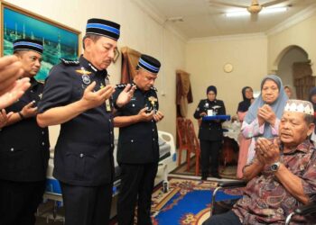 MUHAMMAD Zaki Harun (berdiri, kiri) mengaminkan doa semasa hadir ke rumah Yusoff Hussain pesara polis yang mengalami sakit kronik bagi menyampaikan Pingat Jasa Pahlawan Negara di Kampung Tanjong Mas, Kota Bharu, Kelantan.-UTUSAN/KAMARUL BISMI KAMARUZAMAN