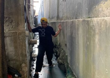 NGADENIN menunjukkan dia terpaksa melalui kawasan parit berlumpur berikutan tembok hotel setinggi 15 meter menghalang akses ke rumahnya. - AGENSI