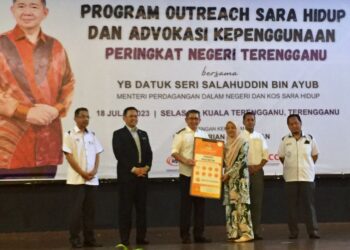 SALAHUDDIN Ayub (tiga dari kiri) menyerahkan replika Inisiatif Rintis Bantuan Tanpa Tunai kepada salah seorang pelajar pada Program Outreach Sara Hidup dan Advokasi Kepenggunaan di Kuala Nerus, petang tadi. - UTUSAN/TENGKU DANISH BAHRI TENGKU YUSOFF