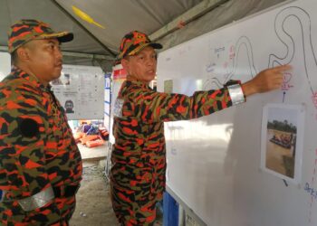 HASSAN 'As'ari Omar (kanan) berbincang pegawainya bagi mengatur strategi operasi mencari dan menyelamat mangsa tragedi kepala air di Pusat Kawalan Operasi, Balai Polis Air Putih, Kemaman, hari ini. - UTUSAN/
NIK NUR IZZATUL HAZWANI NIK ADNAN