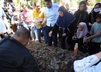 FATIMAH Taha menabur bunga di kubur suaminya di Tanah Perkuburan Islam, Serkat, Pontian, semalam. - UTUSAN/RAJA JAAFAR ALI