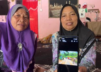 AZIZAH Ishak (kanan) menunjukkan gambar lokasi suaminya maut dipijak gajah di Tanah Tinggi Lojing, Gua Musang. – UTUSAN/AUMI TUAN LAH